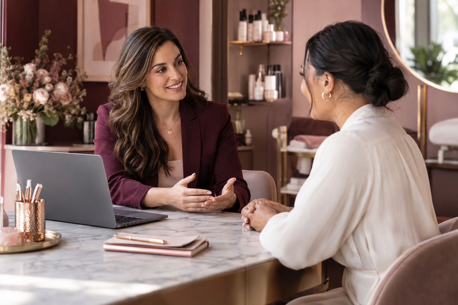Two fictional professionals having a warm conversation beside a laptop in a beauty studio